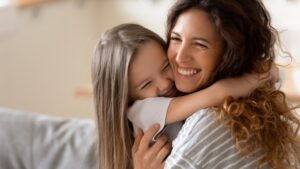 Mother hugging daughter. Both are smiling.